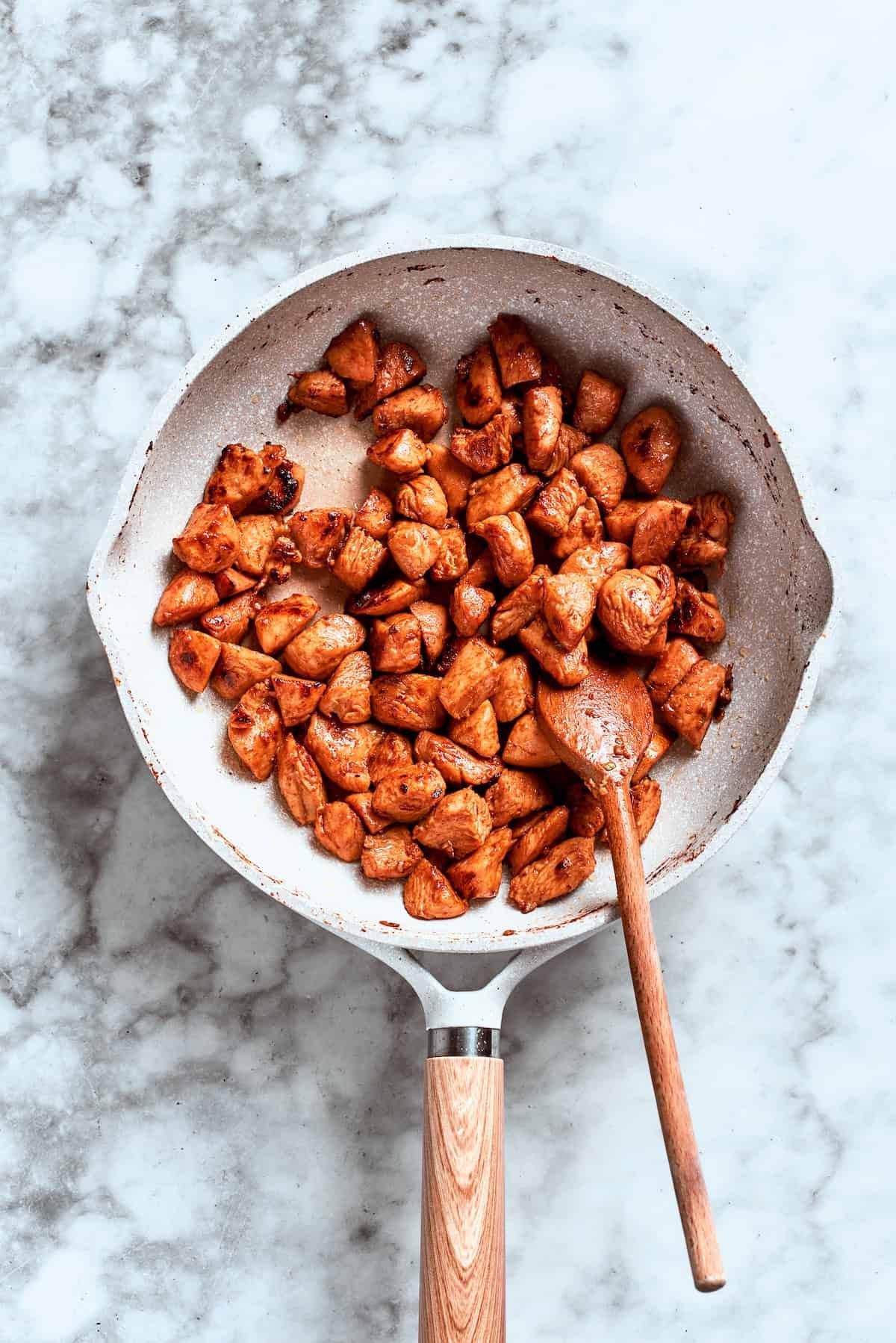 A spoon stirs the chicken as it browns and cooks in the skillet.