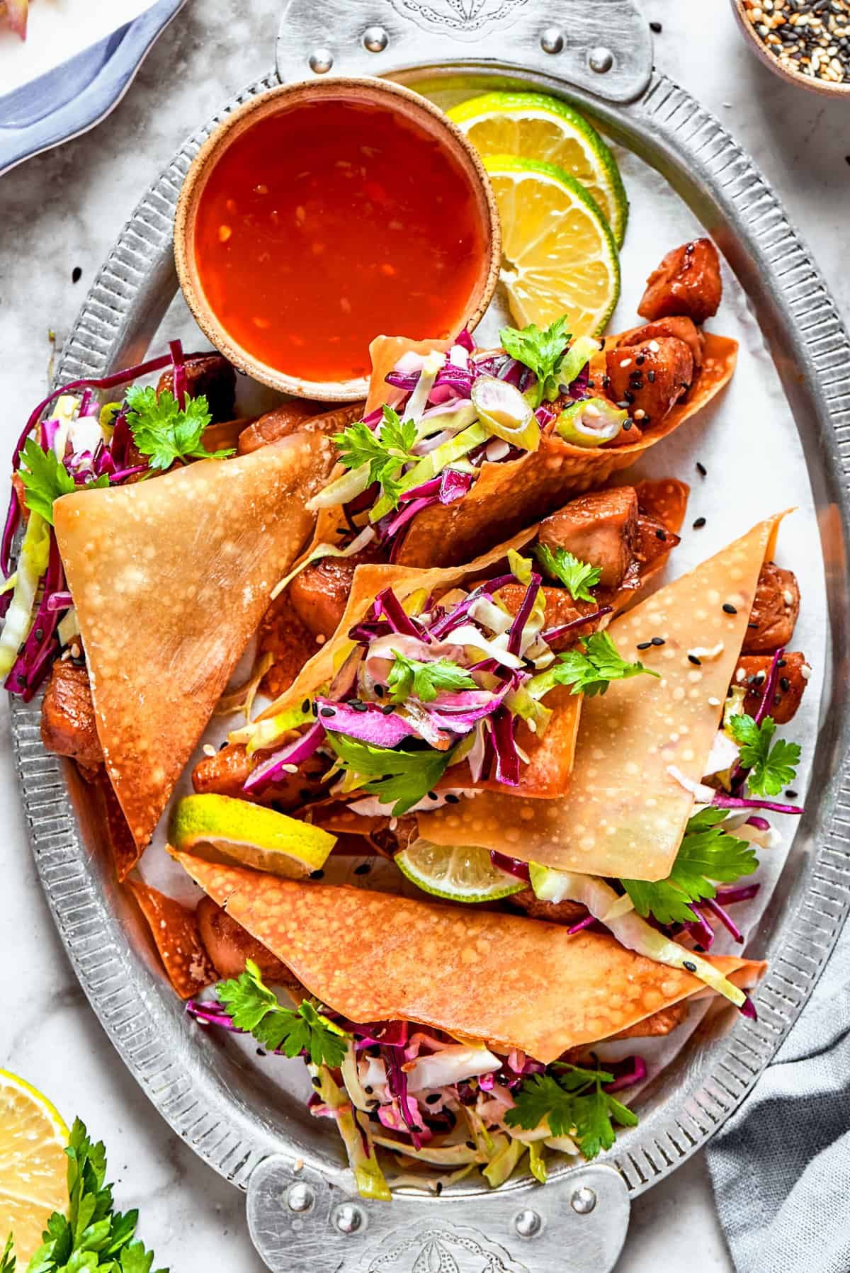 Chicken wonton tacos arranged on an oval platter with a bowl of sauce set right next to the tacos.