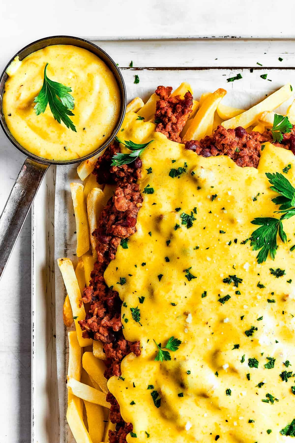 Homemade chili cheese fries with dipping sauce and a blue tea towel.