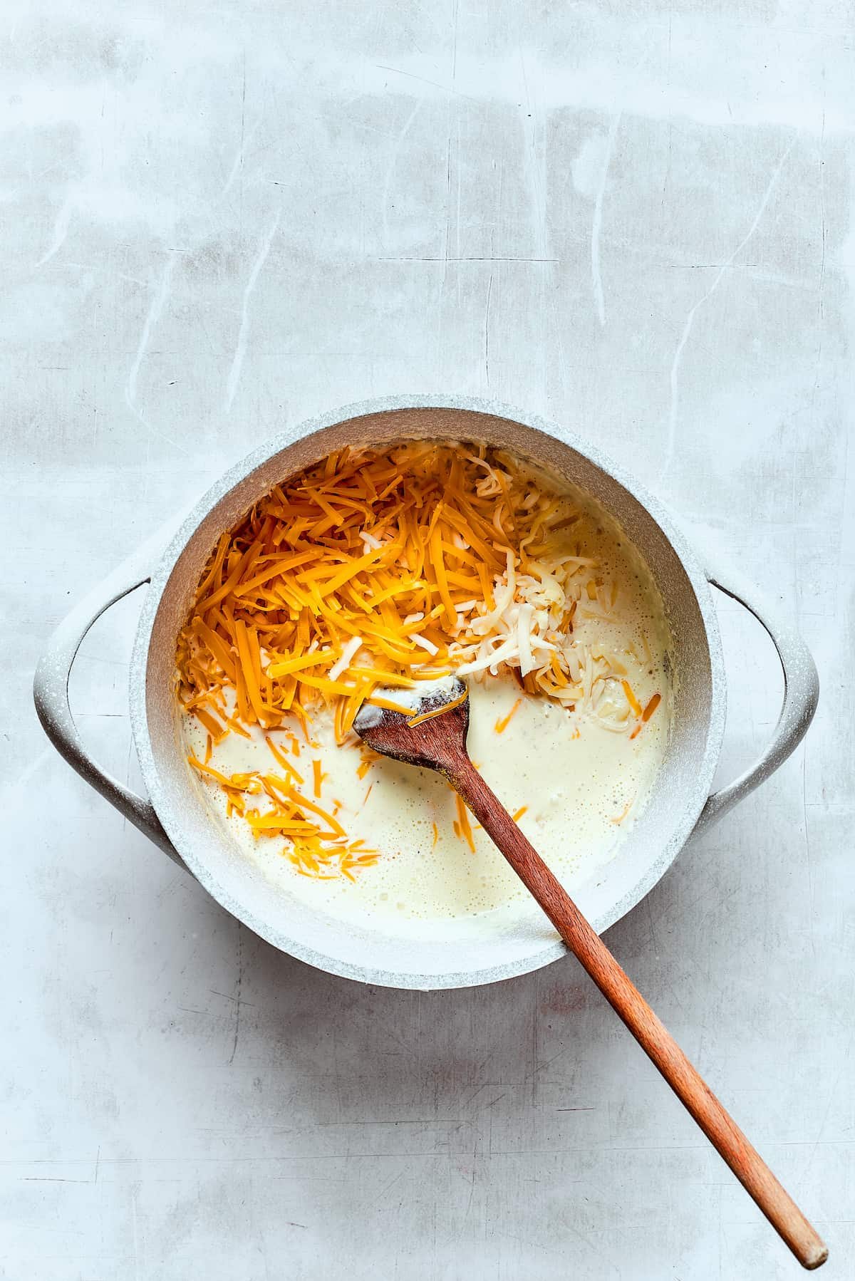 Stirring cheddar cheese into a hot cream mixture to make cheese sauce.