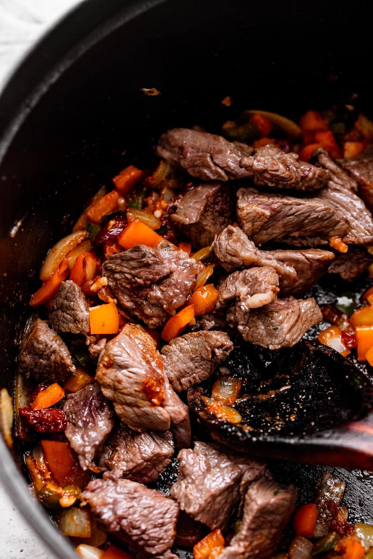 browning pieces of chuck roast and diced veggies inside a dark skillet.