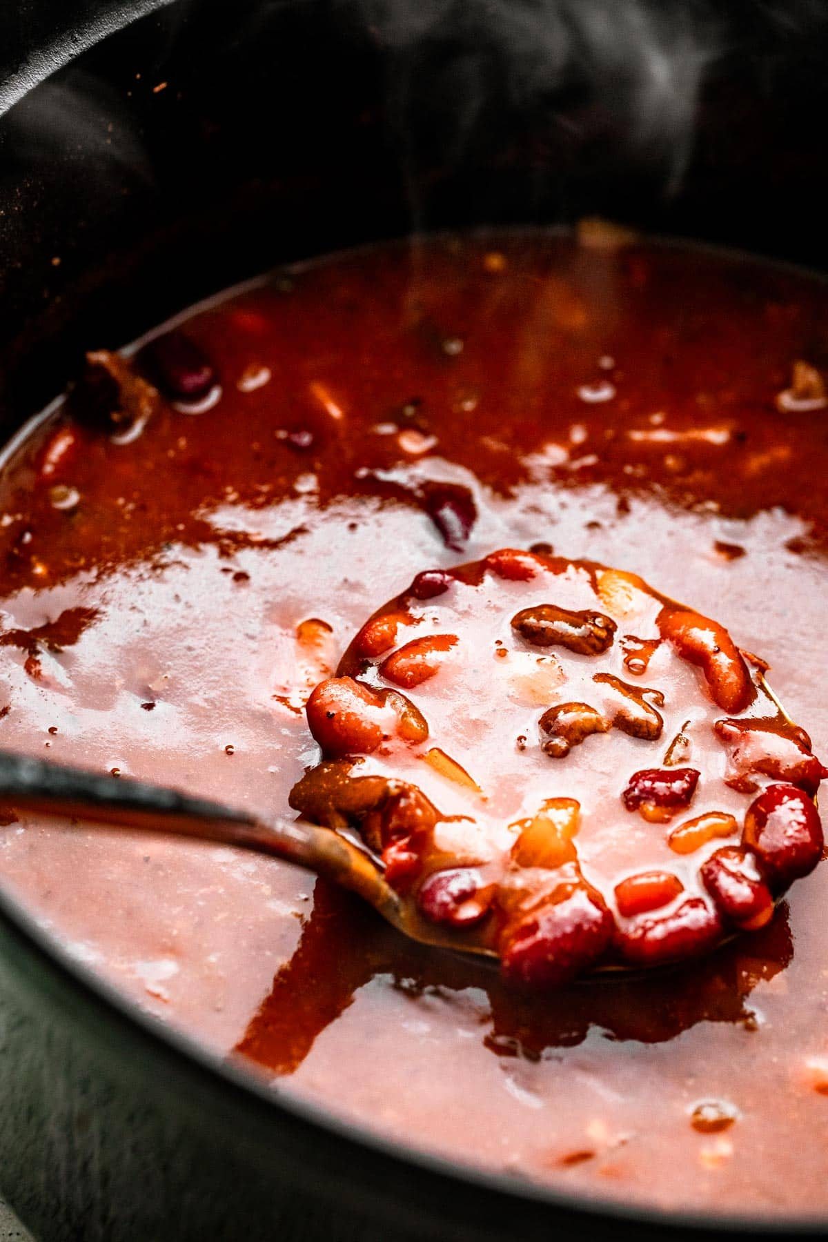 a ladle spooning out chili con carne from a dark colored pot.