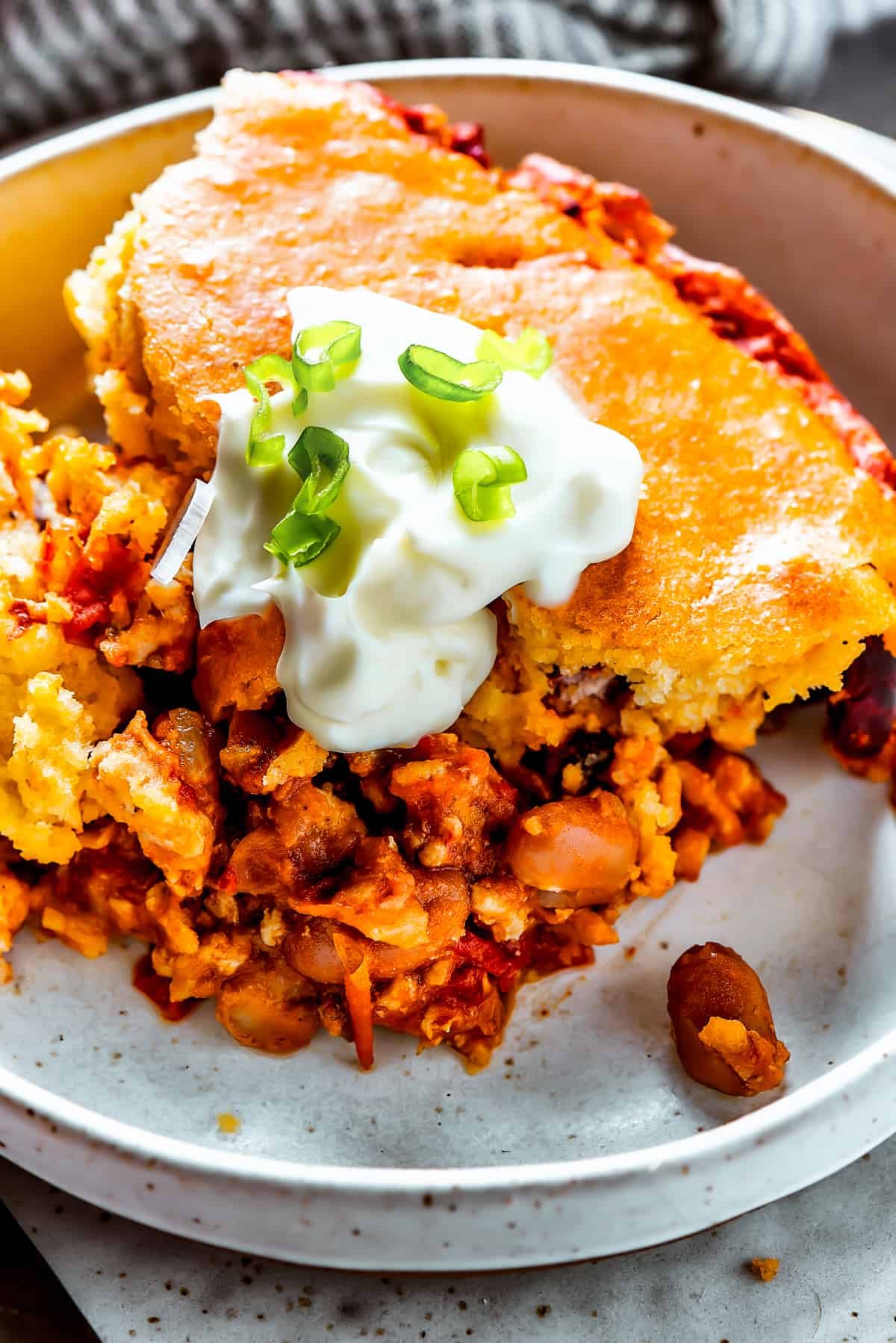 Chili cornbread casserole on a dinner plate with sour cream and scallion.
