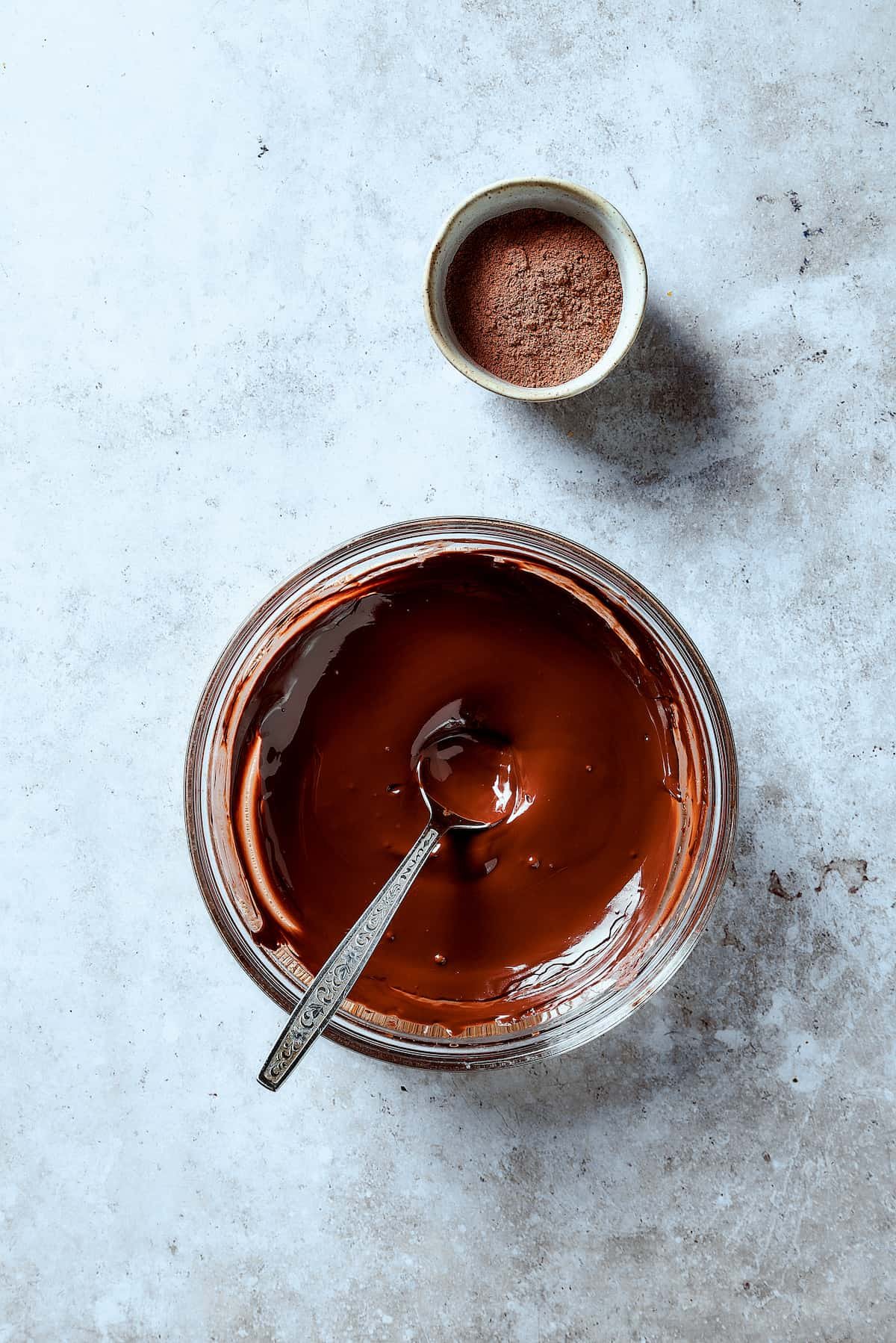 Melted chocolate in a mixing bowl next to a dish of cocoa powder.
