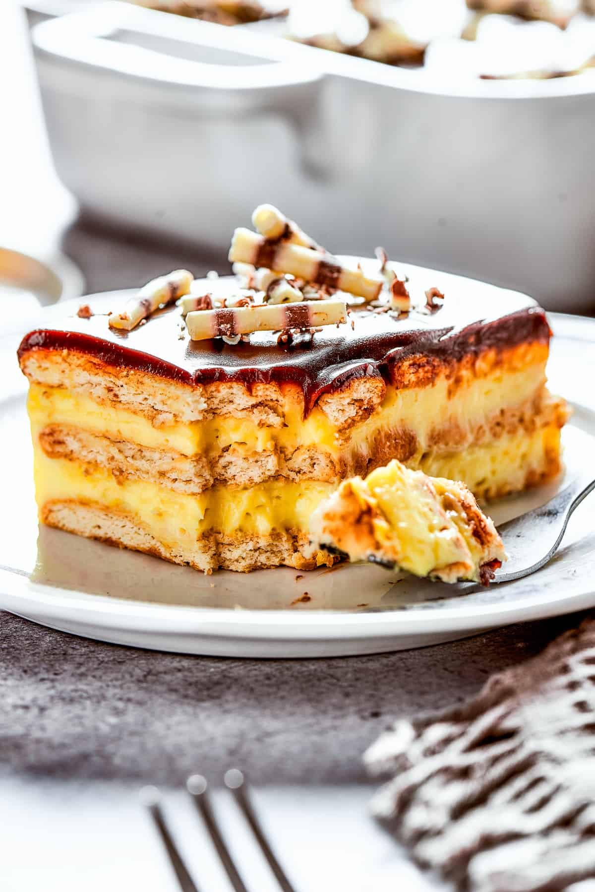 A slice of chocolate eclair cake on a plate, with a fork on the plate with a bite of cake.