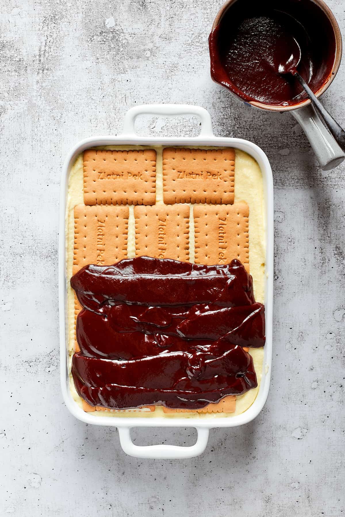 Overhead view of chocolate ganache half-spread over cookies in a baking dish.