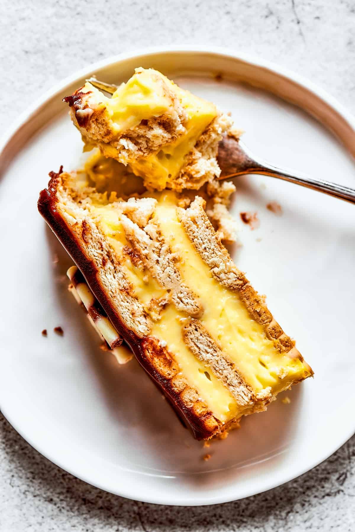 Overhead view of a piece of chocolate eclair cake on a plate, with a bit of it broken off with a fork.