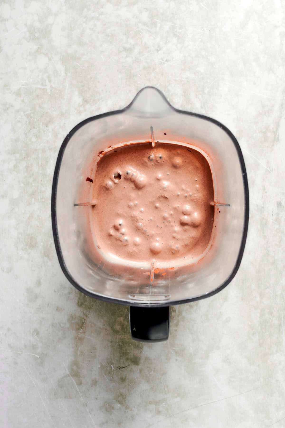 A blender holds a blended chocolate milkshake.