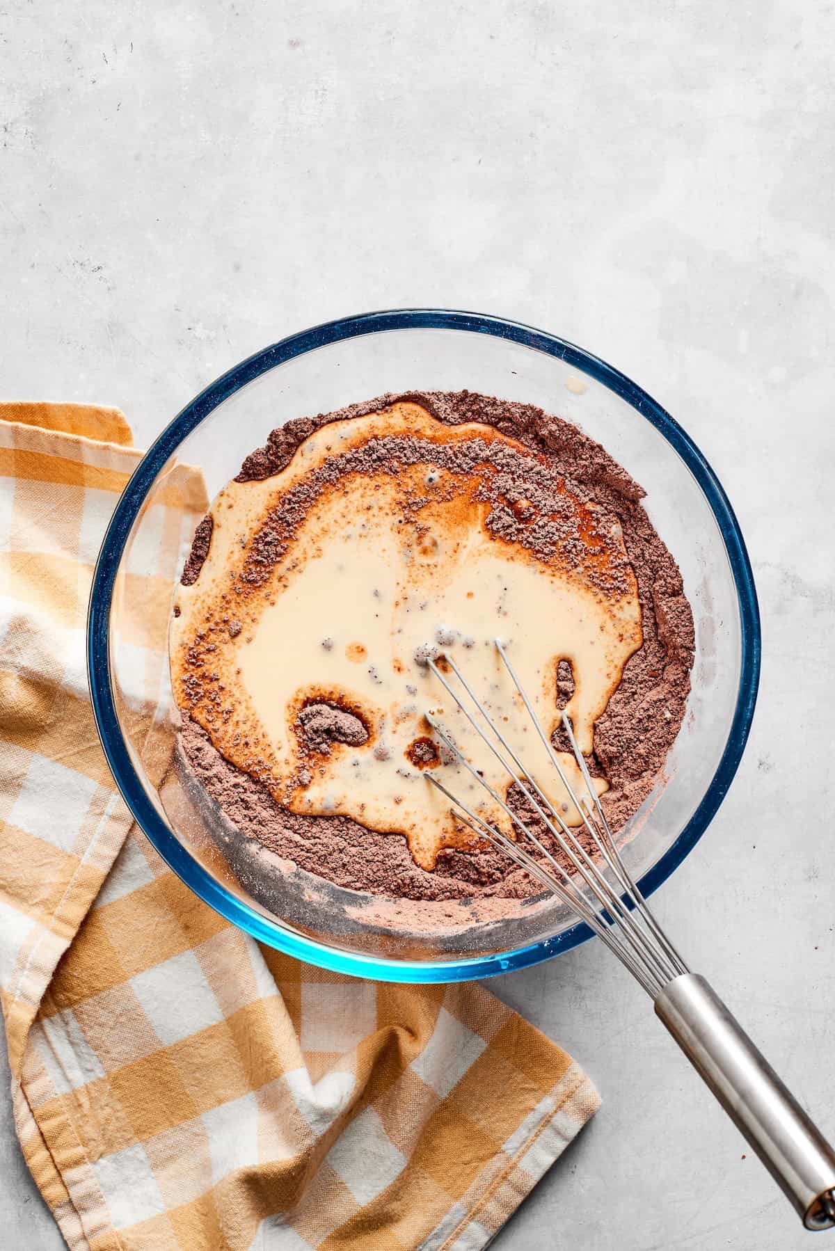 Dry and wet ingredients for chocolate muffins are whisked together in a bowl.