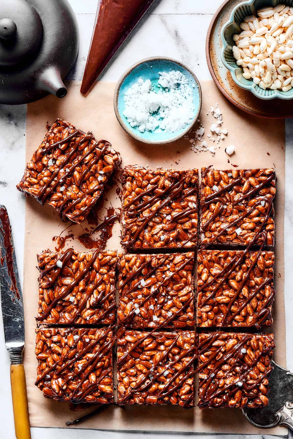 Squares of chocolate rice krispie treats next to a bowl of flaky sea salt.