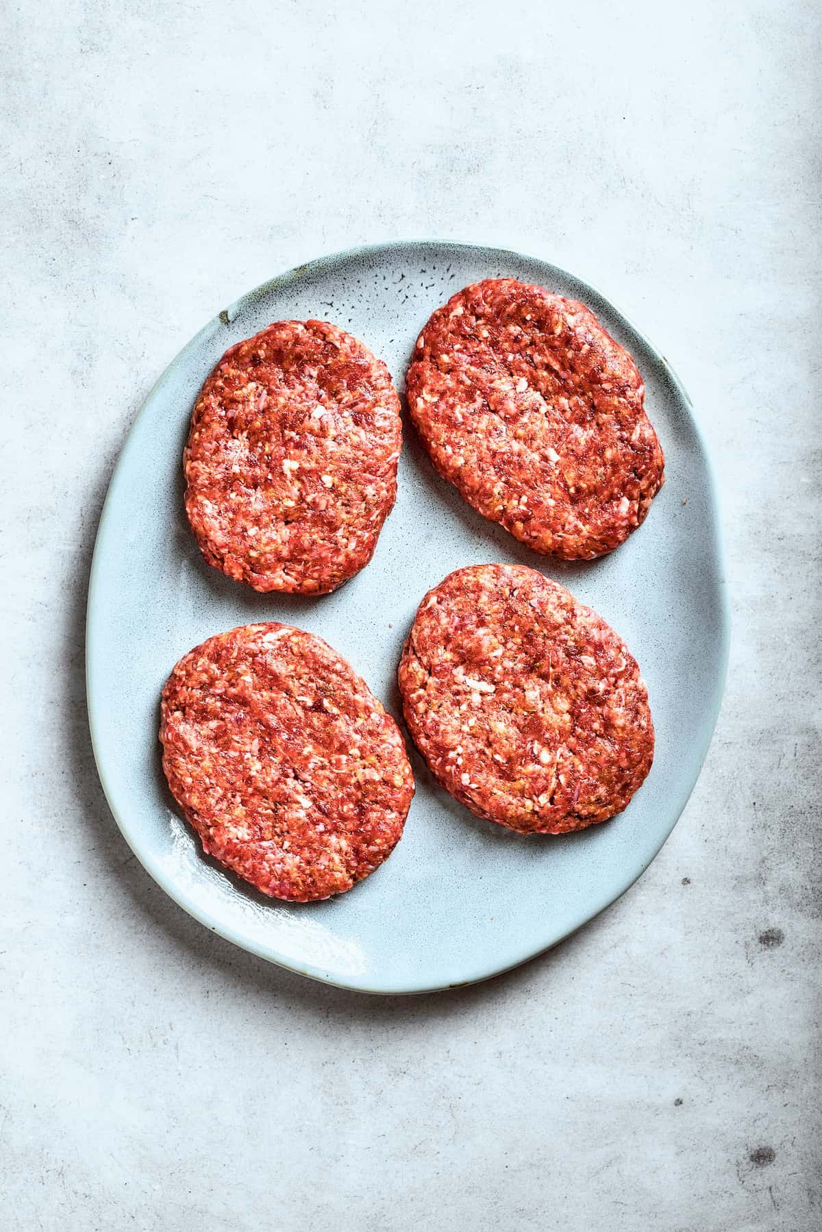 Four beef patties on a platter.