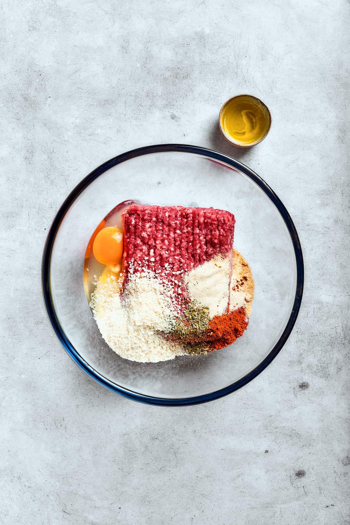 Ground beef, an egg, and breadcrumbs in a glass bowl.