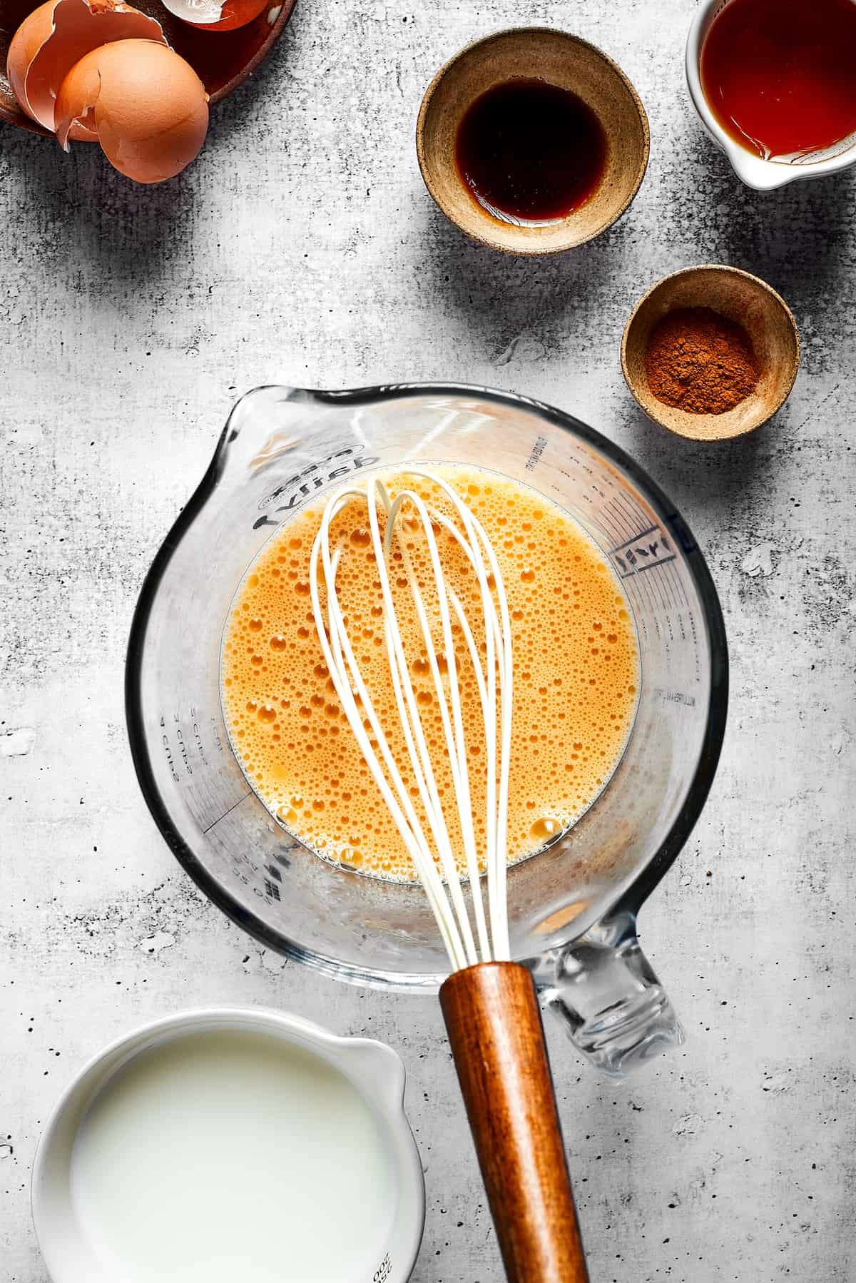 A pyrex with an egg and milk mixture with a whisk in it, next to some bowls