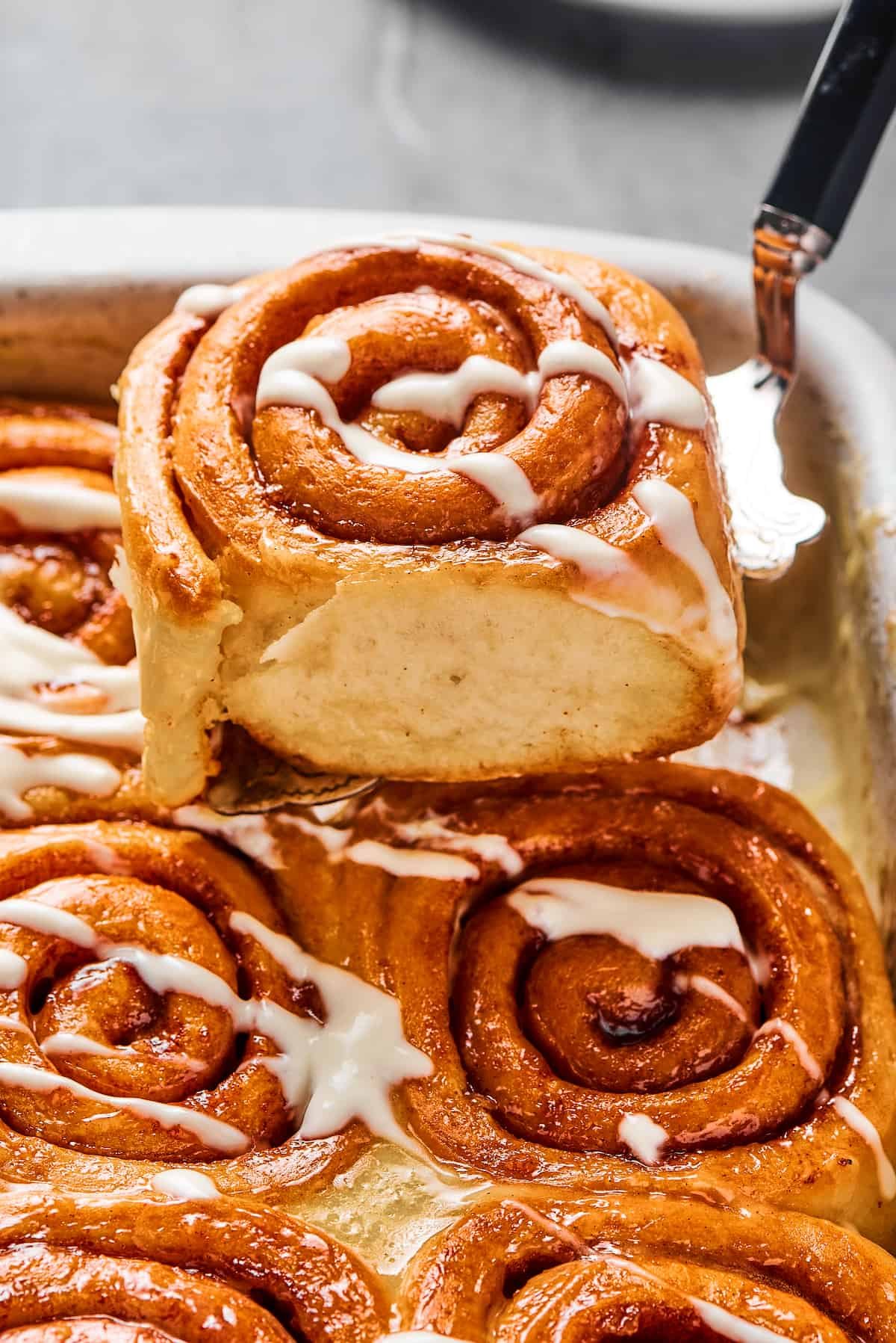 A cinnamon bun lifted from a pan, to show the texture of the torn side of the roll.