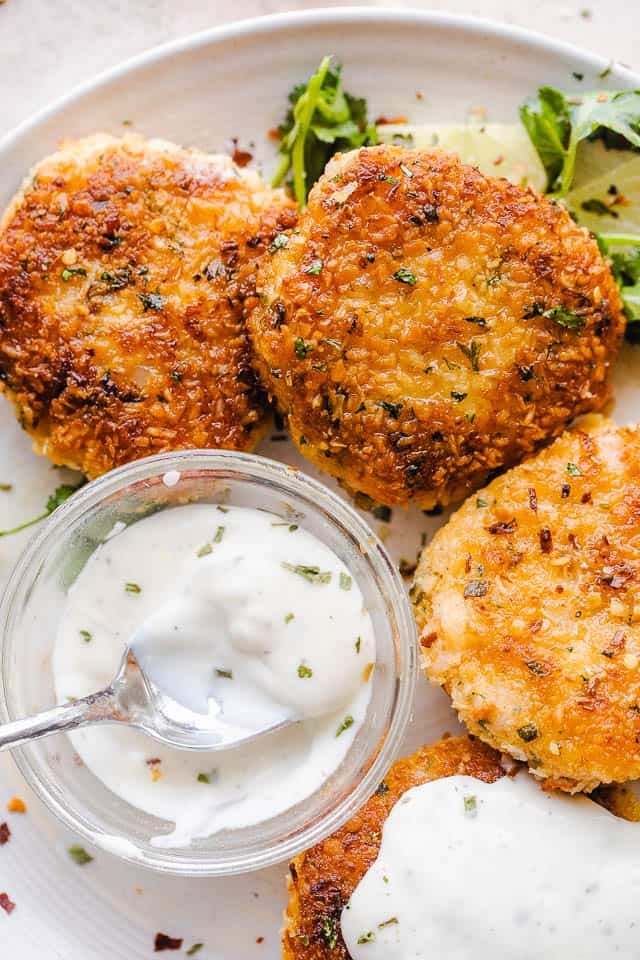 overhead shot of plated shrimp cakes on a white serving plate and a bowl of sauce