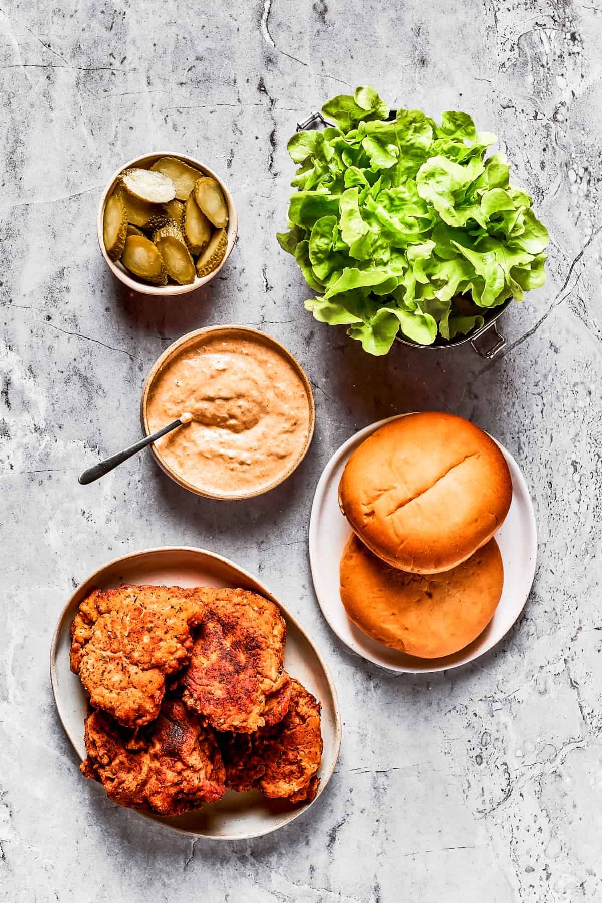 From top: sliced pickles, lettuce, spicy mayo, buns, and fried chicken.