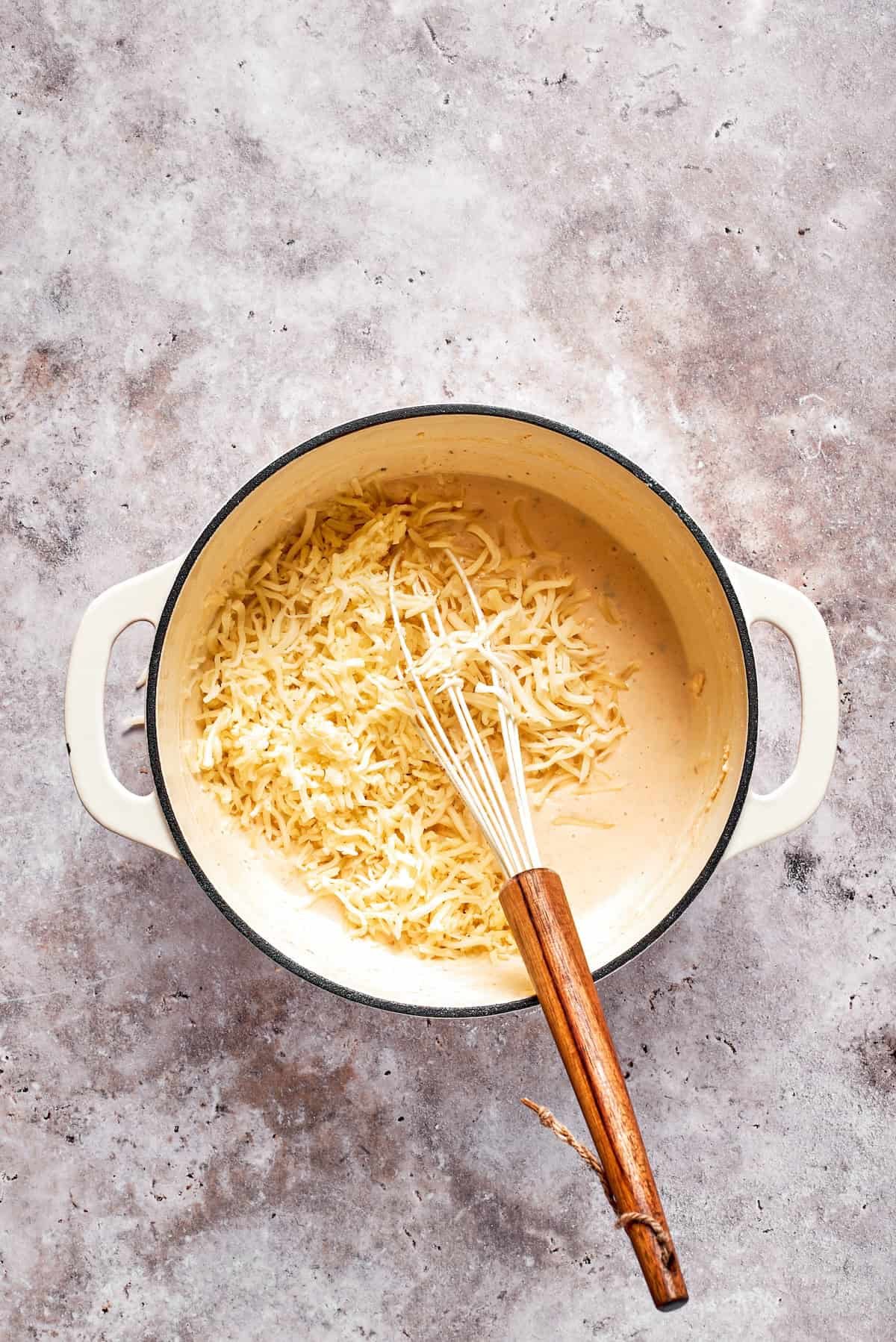 Shredded cheese is added to a pot of sauce.