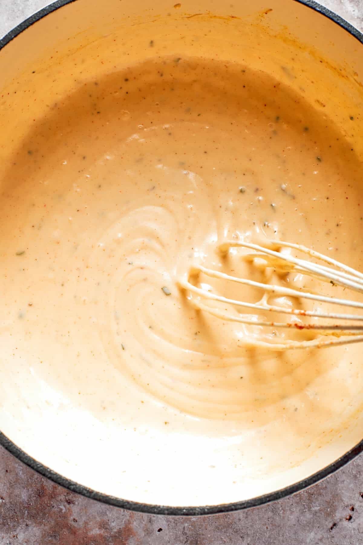 A whisk stirs a pot of cheese sauce.