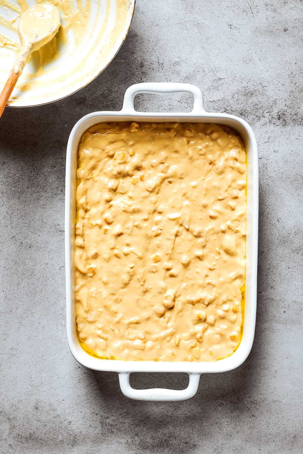 Corn souffle batter is shown in a white baking pan.