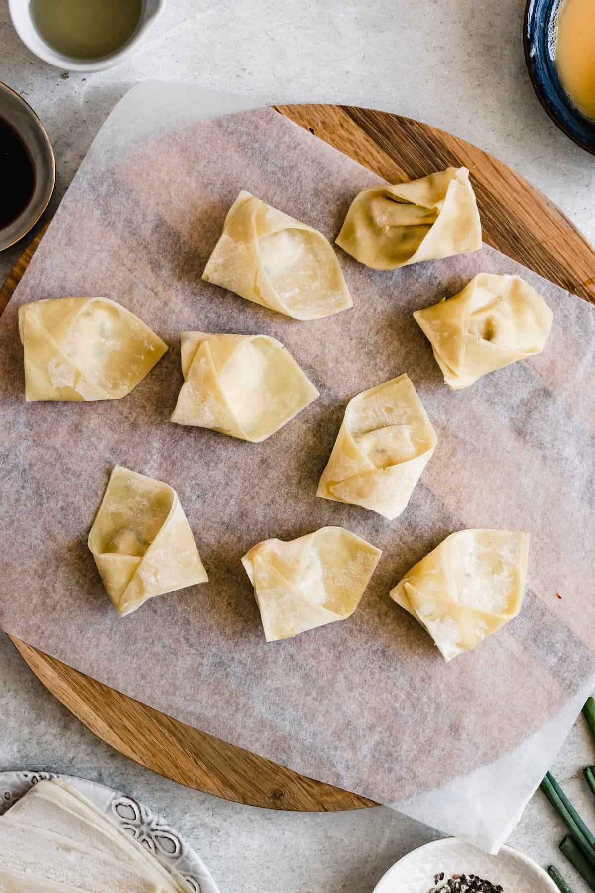 Filled and wrapped wonton wrappers and set on a cutting board.
