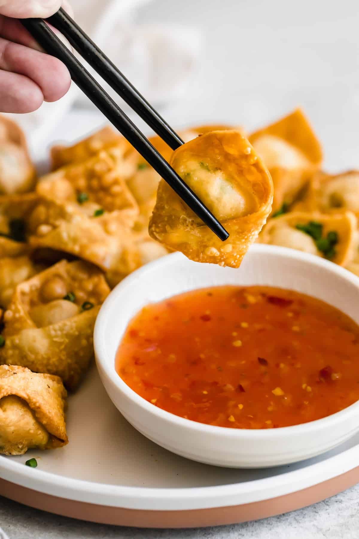 holding chopsticks and dipping crab rangoon wonton in dipping sauce