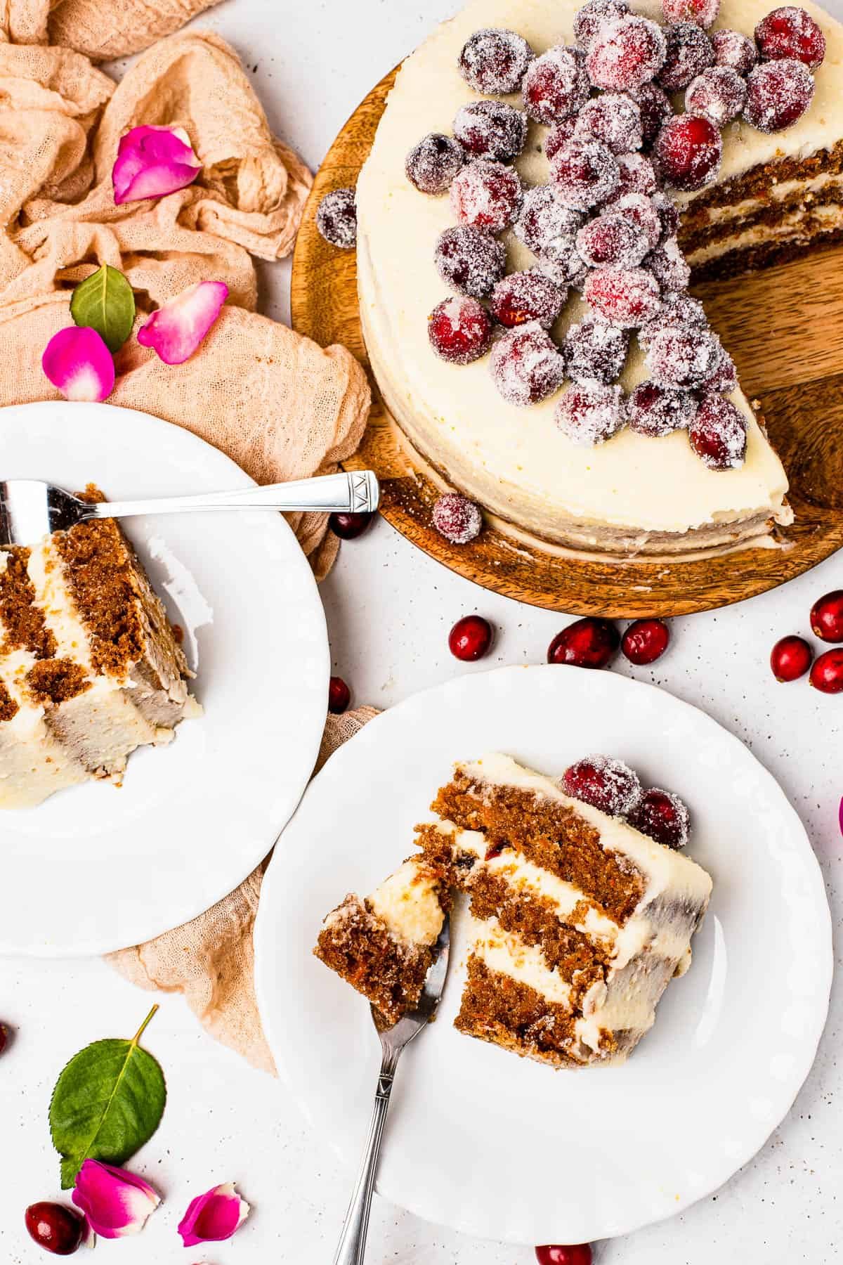Slices of sugared cranberry layer cake on dessert plates, next to the remaining cake on a cake stand.