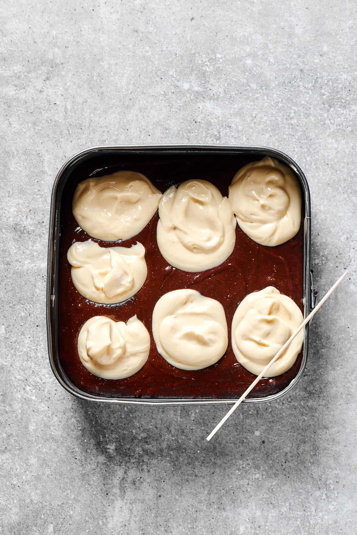 Dollops of white cream cheese on a pan of brownie batter.