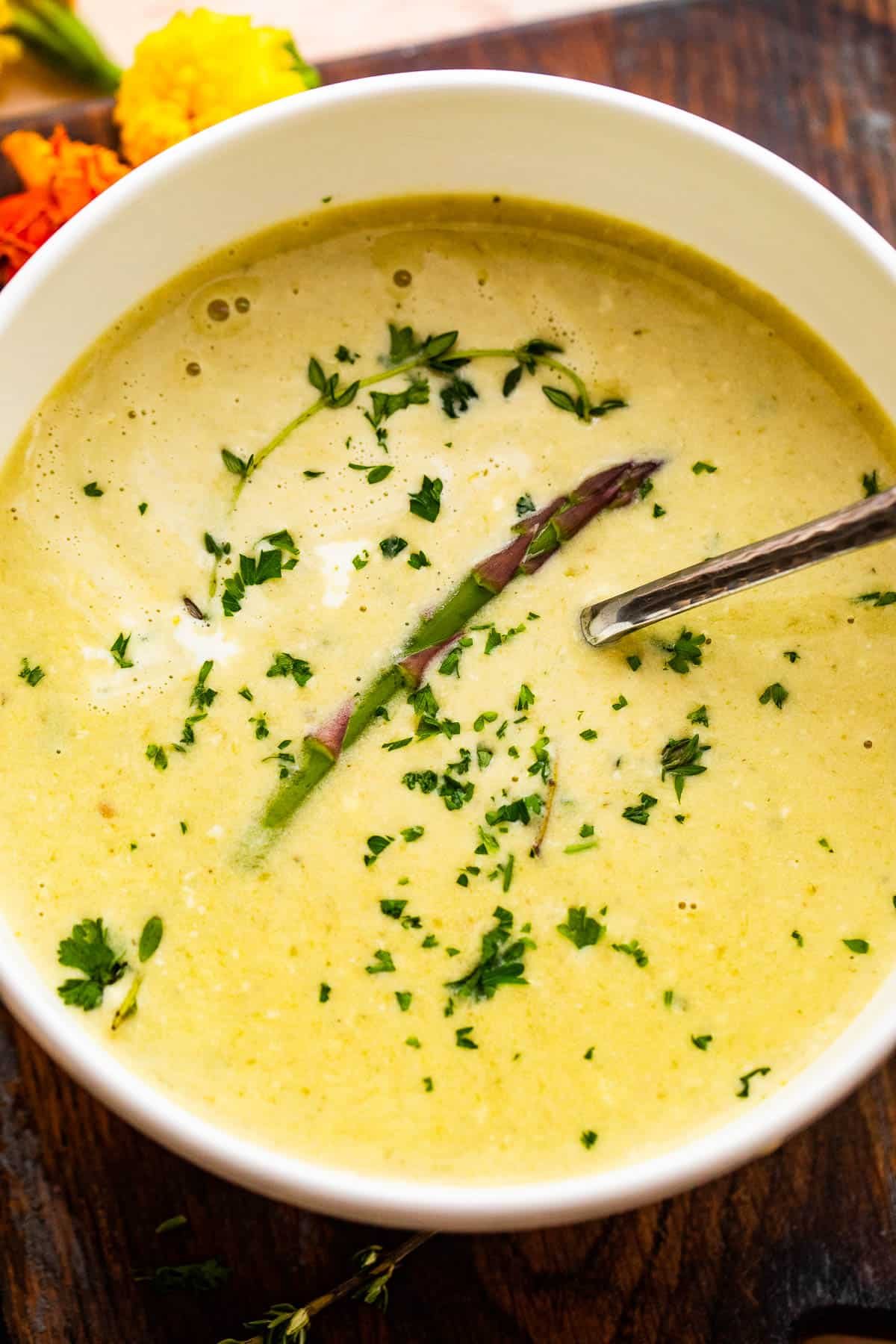 Overhead shot of Cream of Asparagus Soup served in a white bowl garnished with an asparagus spear and parsley.