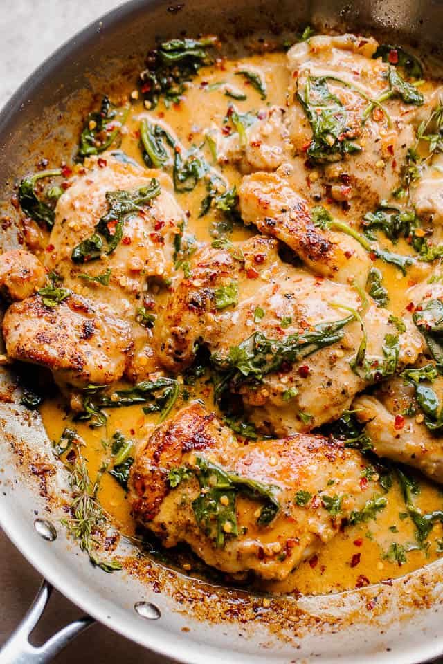overhead shot of a silver skillet with boneless skinless chicken thighs in a creamy sauce with spinach