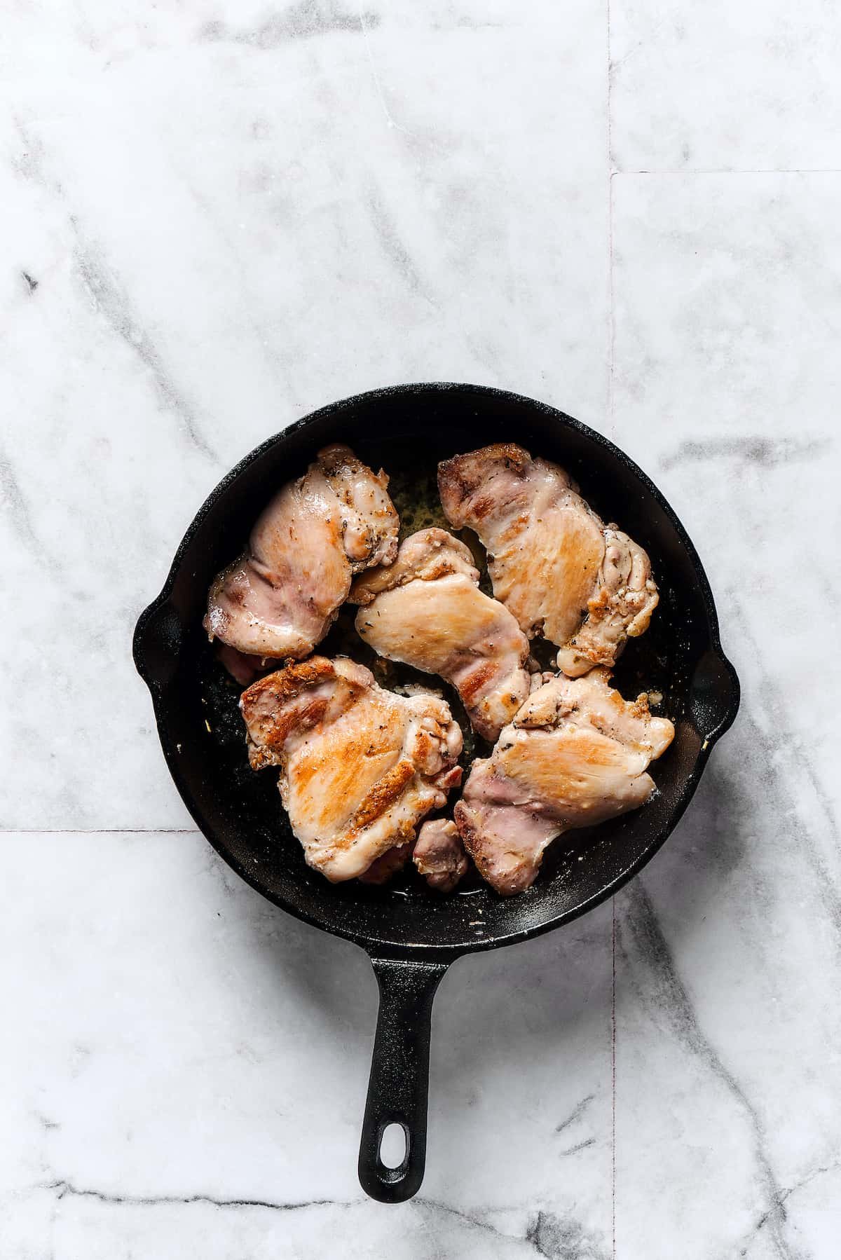 Chicken thighs browning in a skillet.