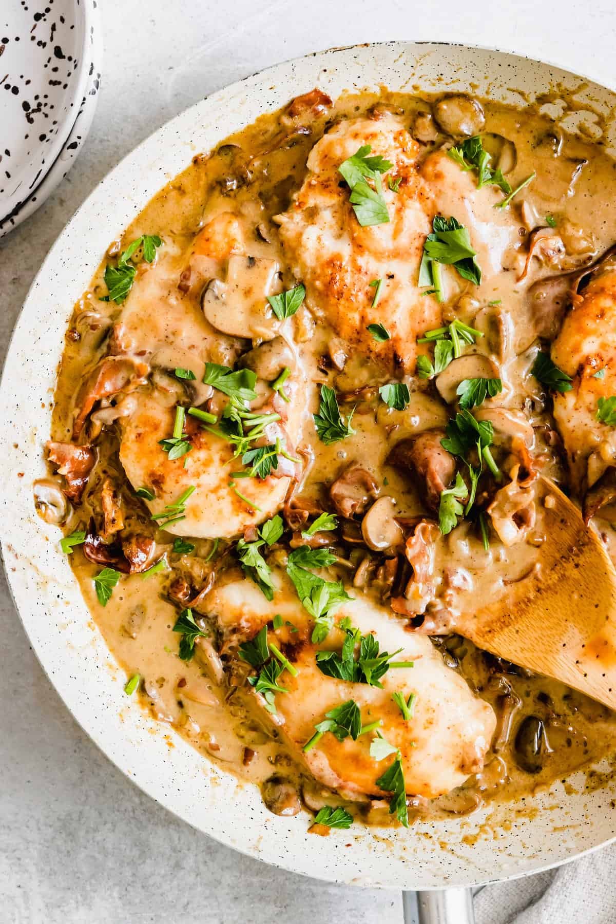 Chicken marsala in a white pan with a wooden spoon
