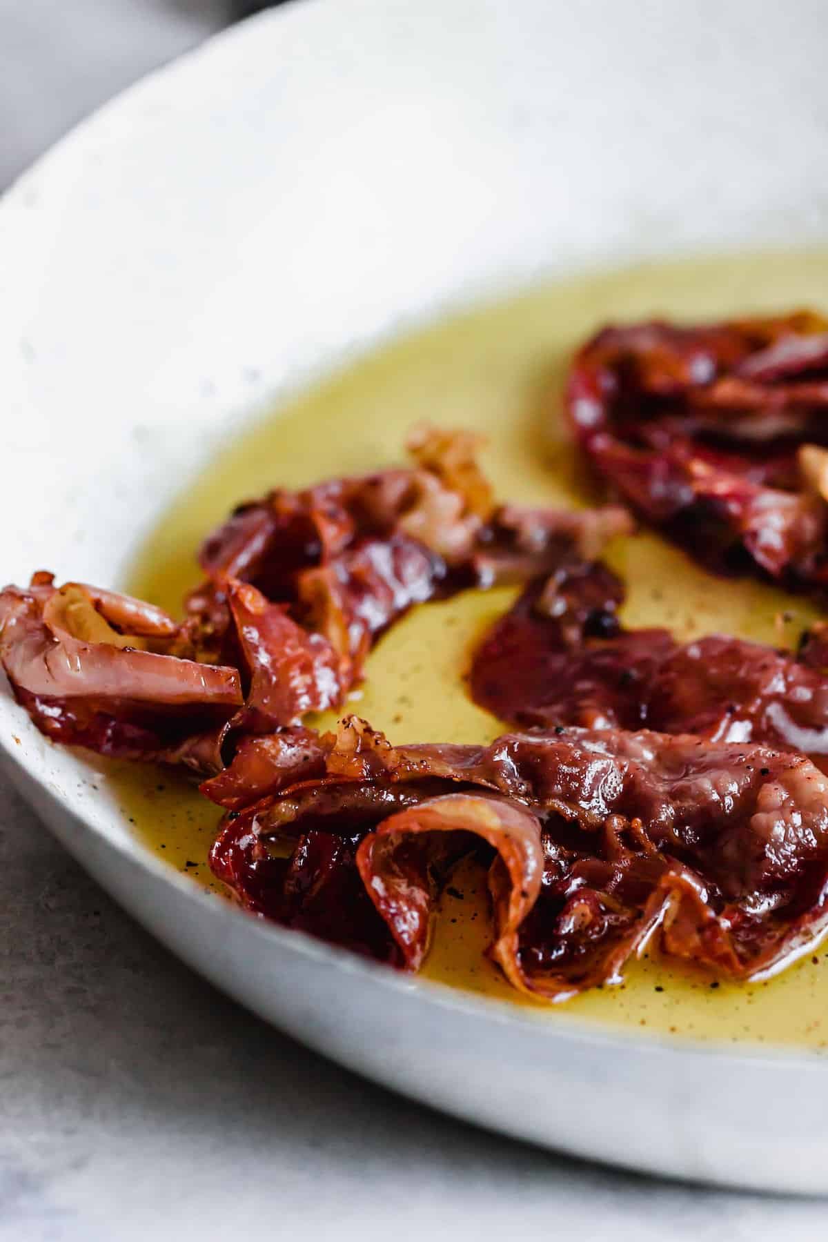 Proscuitto frying in oil in a saute pan.