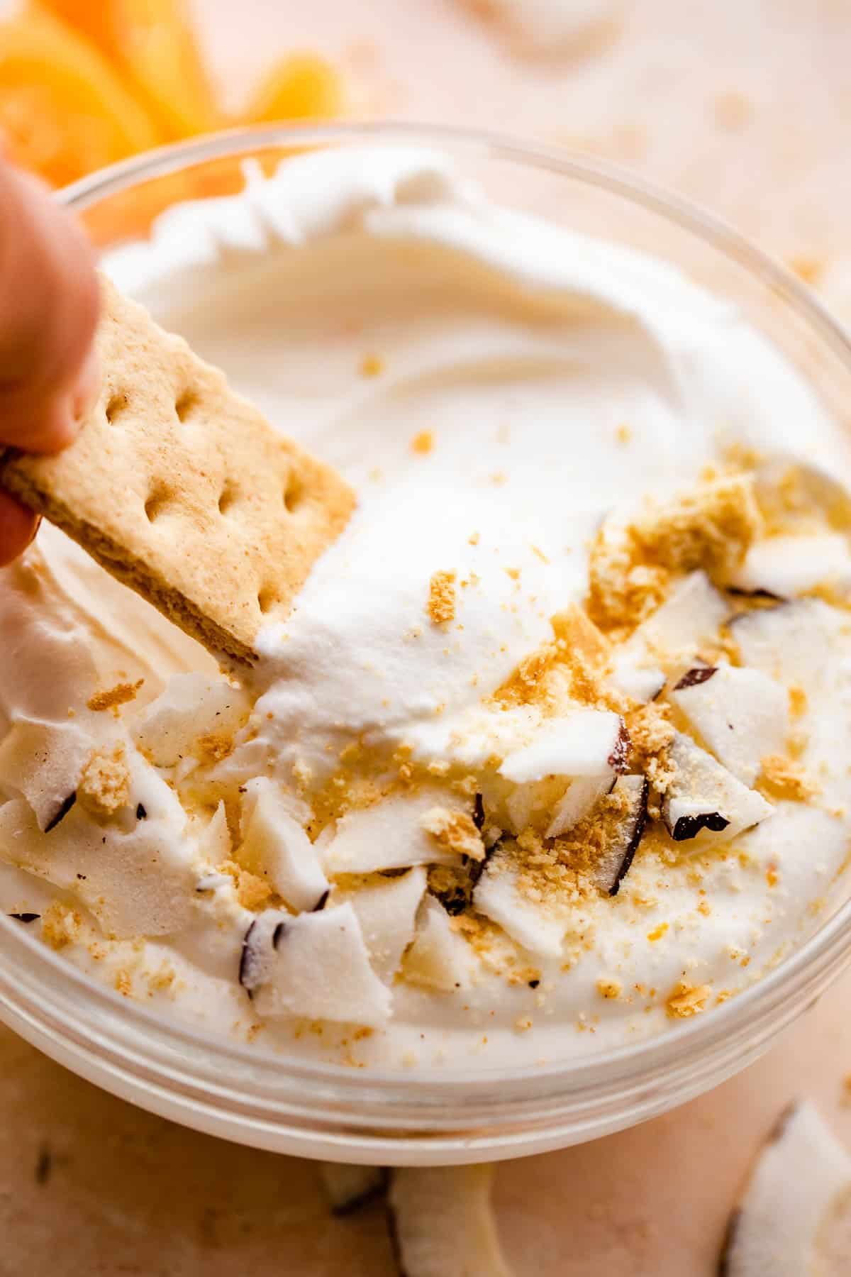 graham cracker dipping into a creamy coconut fruit dip topped with cookie crumbs and coconut shavings.