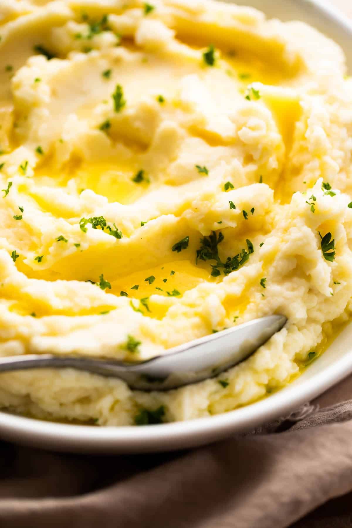 close up side shot of creamy mashed potatoes garnished with melted butter and parsley