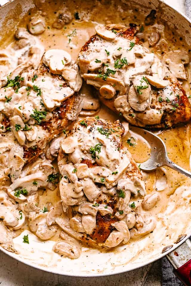 Creamy mushrooms spooned over chicken in a skillet garnished with fresh herbs