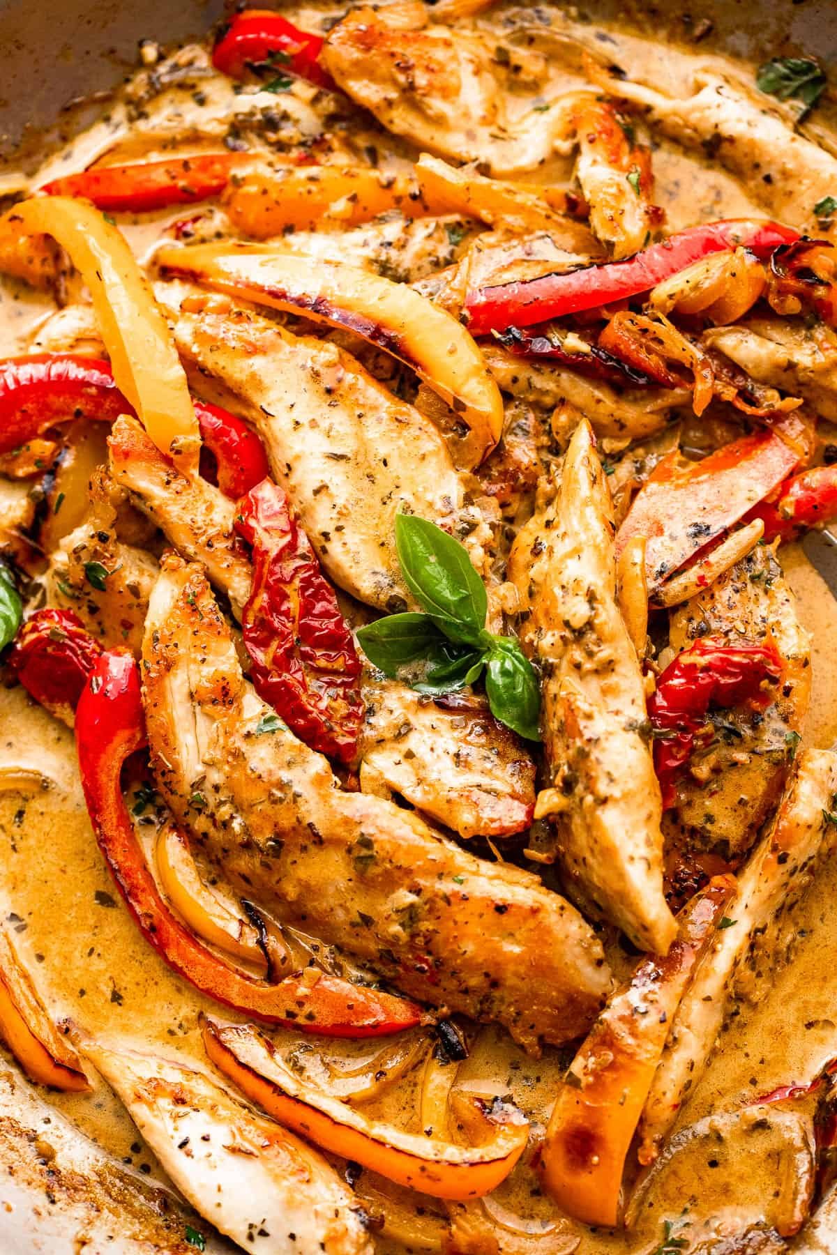 close up shot of chicken strips, bell pepper strips, and creamy pesto sauce