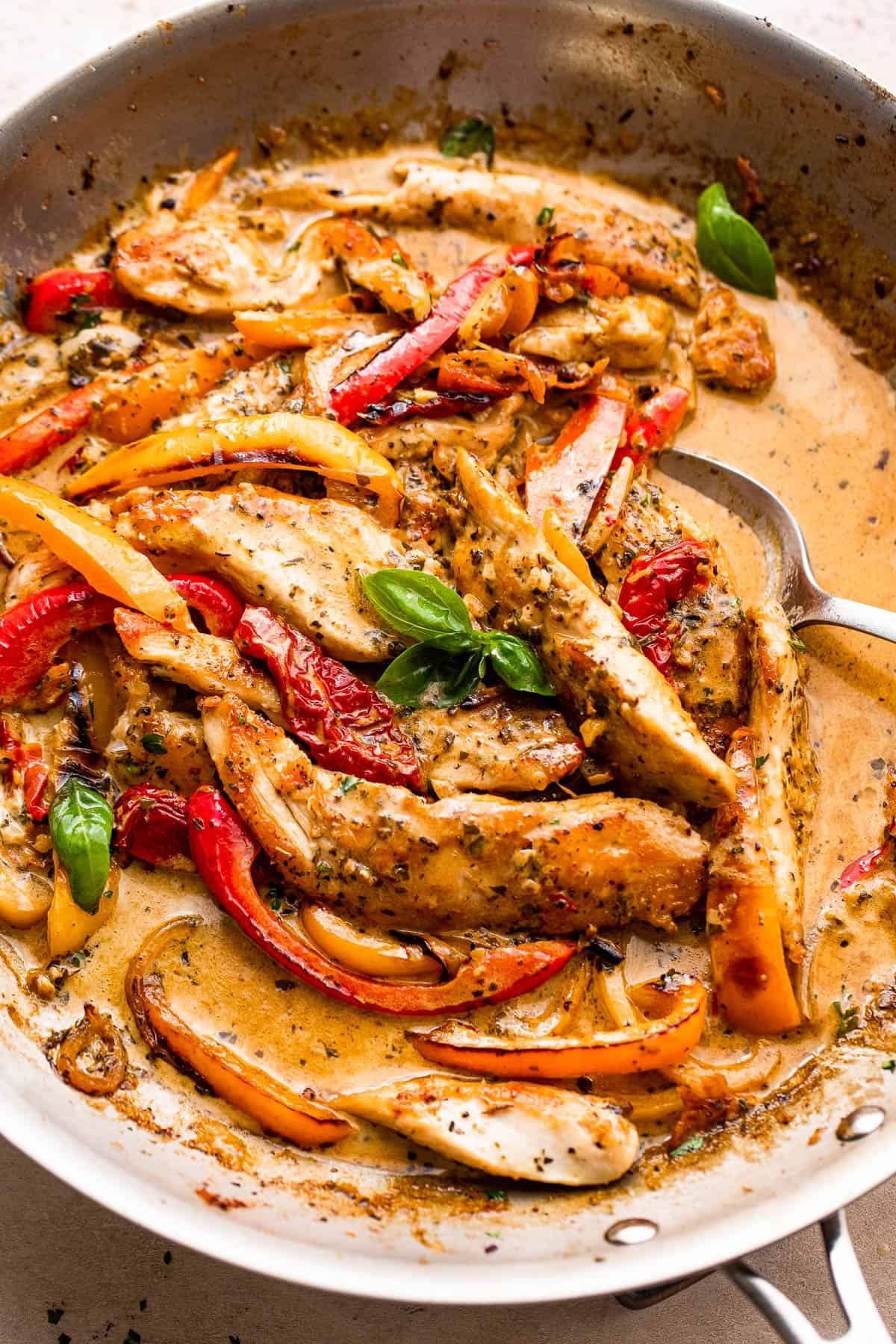 overhead shot of a skillet with creamy pesto chicken strips, peppers, and cream sauce