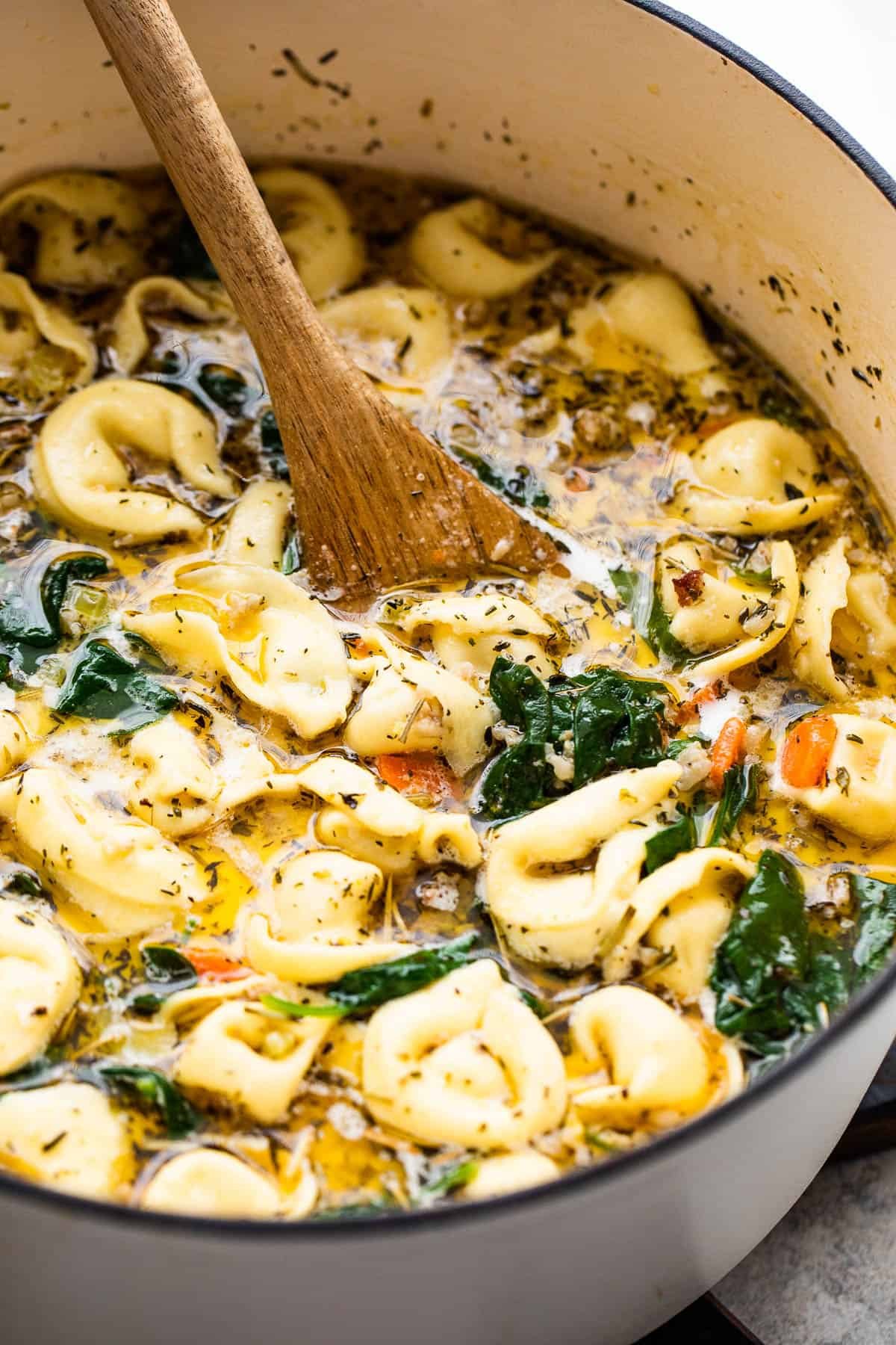 stirring through tortellini soup with a wooden spoon
