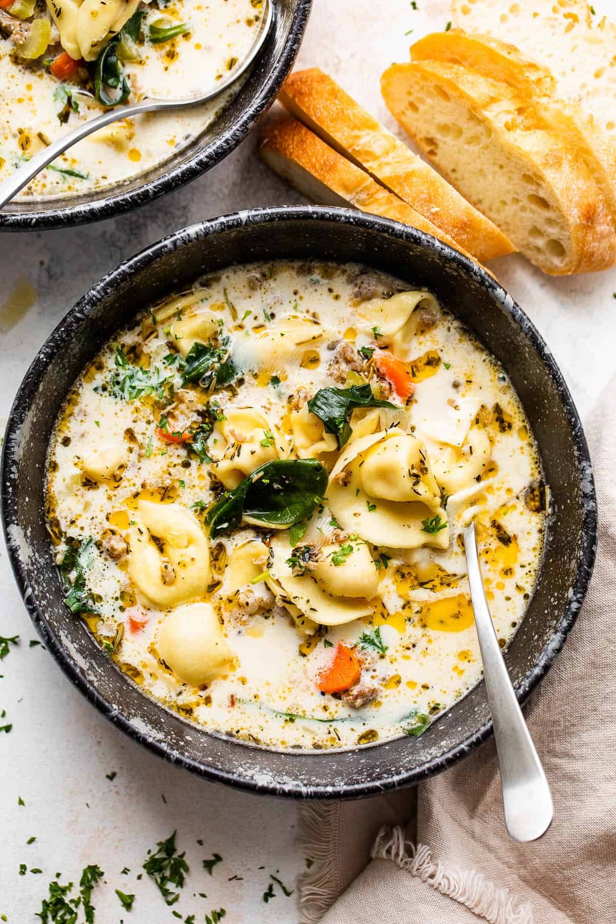 overhead shot of creamy tortellini sausage soup in a black soup bowl with a spoon inside