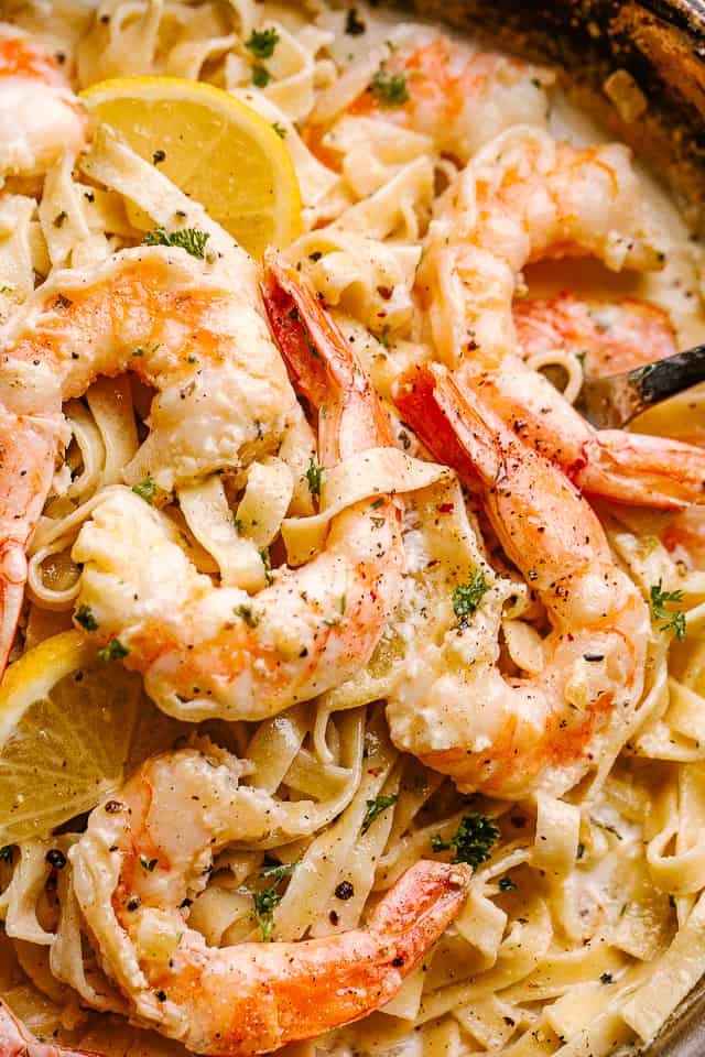 Close up of Creamy Shrimp Alfredo Pasta in a pan garnished with lemon wedges.