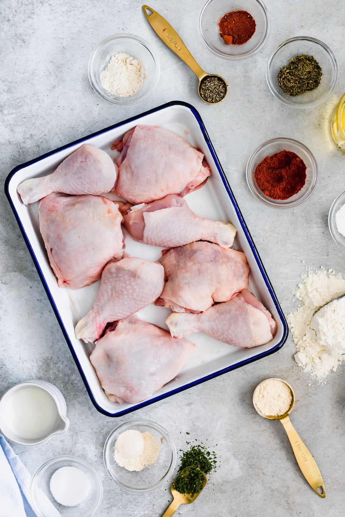 Eight Chicken Thighs and Drumsticks in a White and Blue Pan Surrounded by Herbs, Spices and Buttermilk