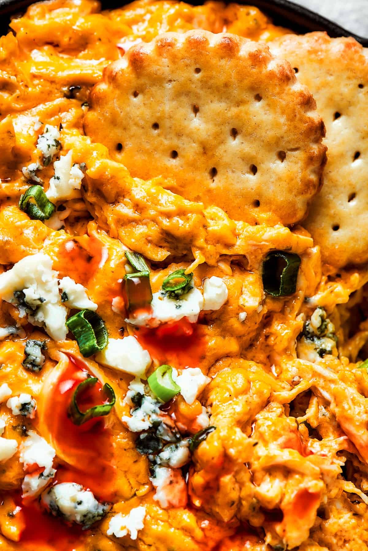 Close-up image of crackers dipped into a dish of buffalo dip.