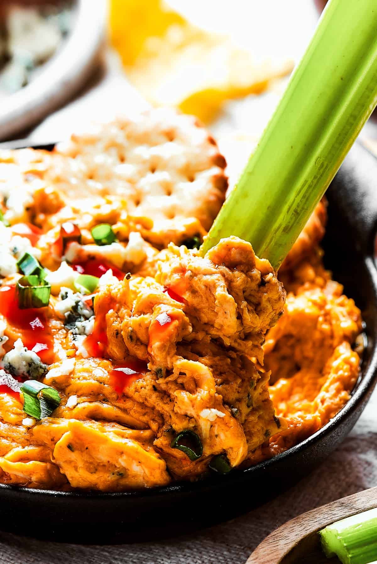 Close-up shot of buffalo chicken dip garnished with blue cheese and green onions and a celery stick dipping in.