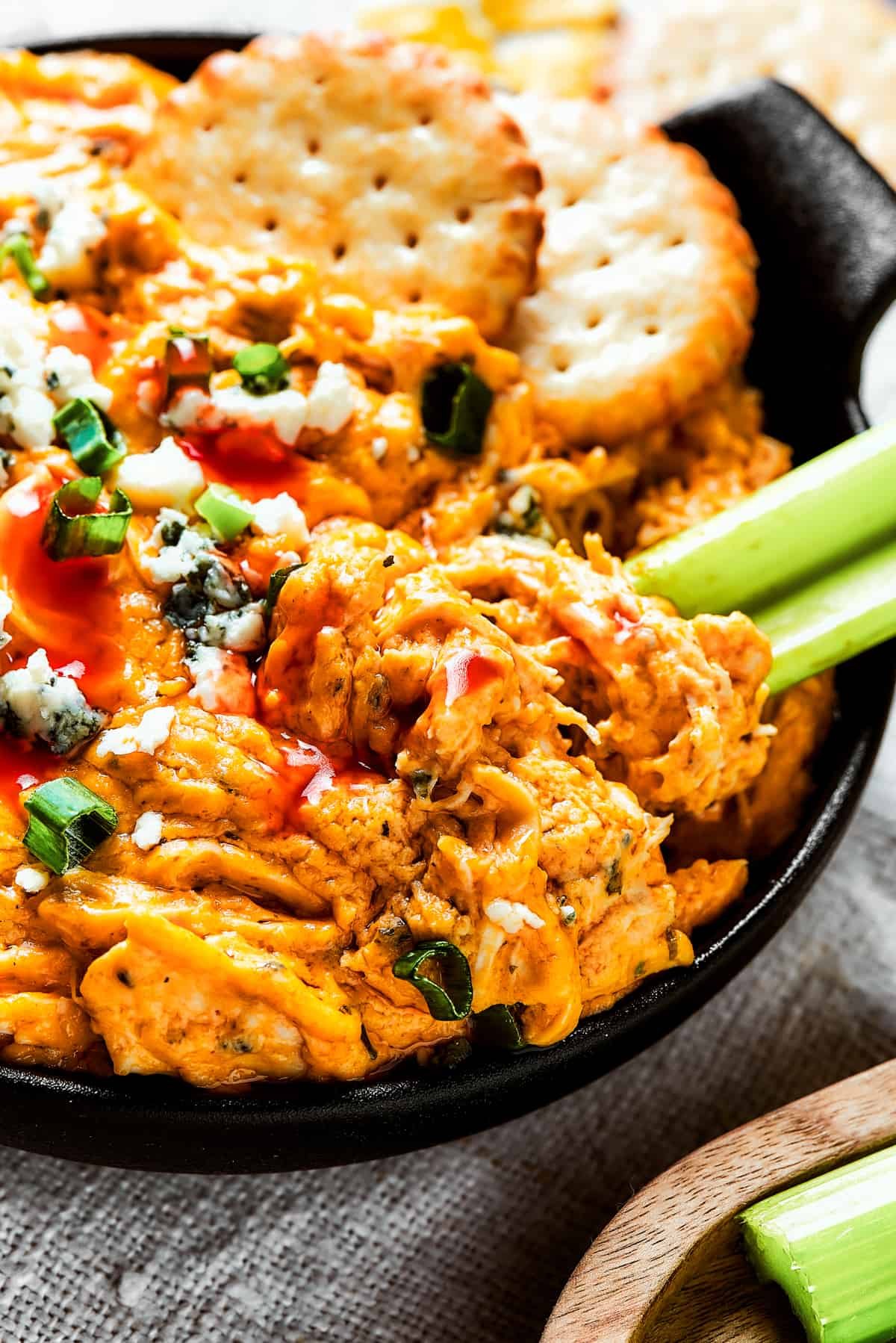 A small, two-handled dish of crockpot buffalo chicken dip with celery and crackers.