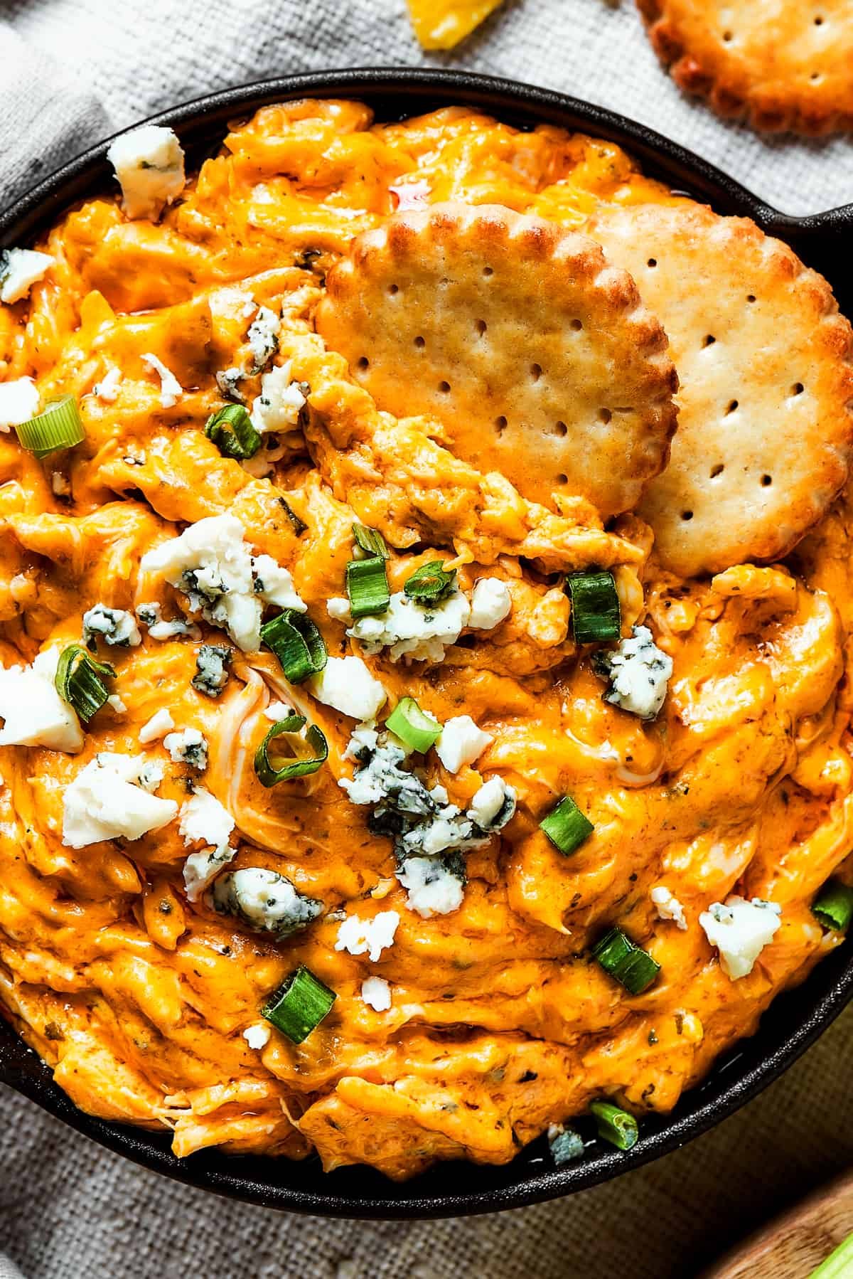 Two crackers dipped into a dish of buffalo dip.