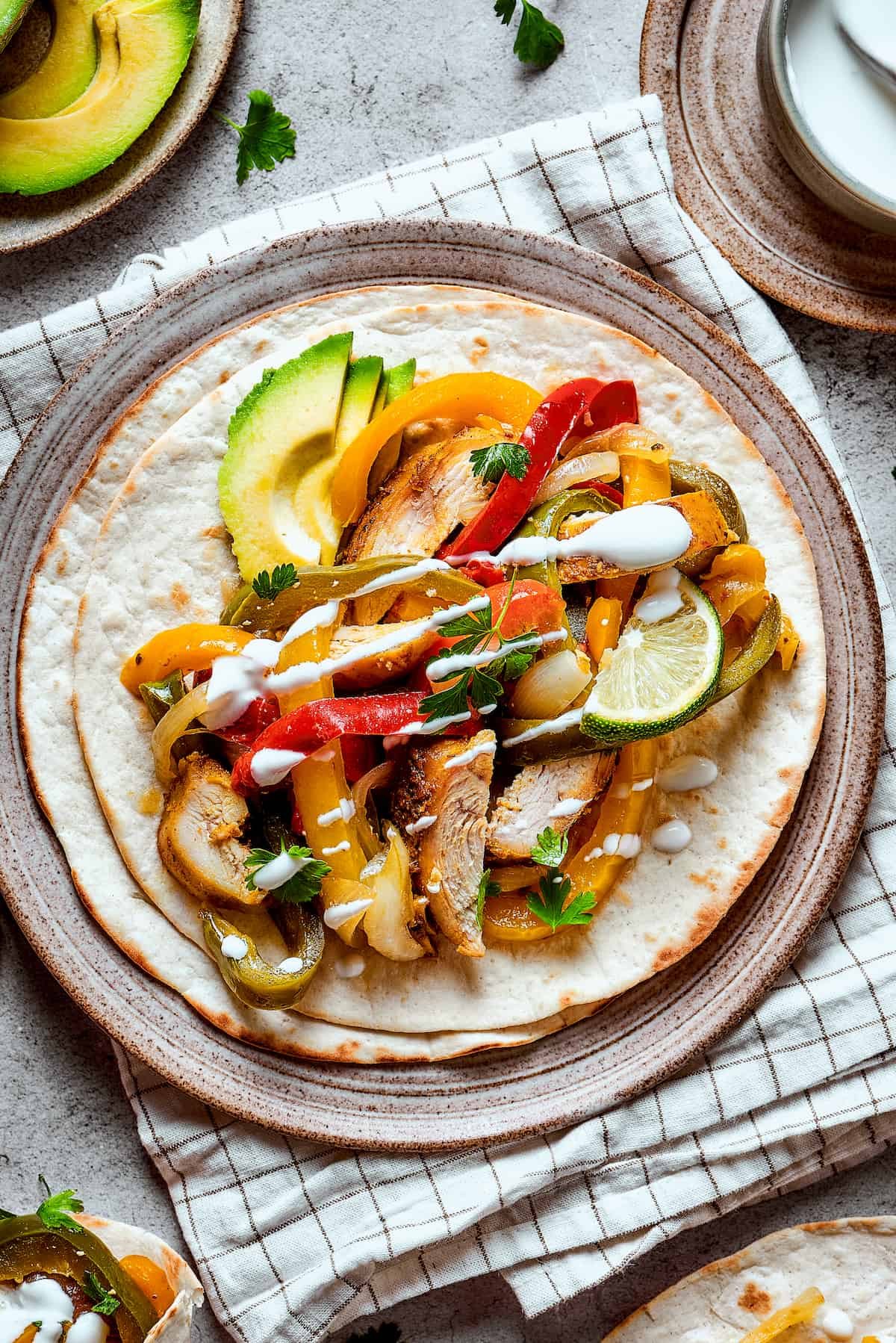 Crockpot chicken fajitas plated ad topped with lime, avocado, and sour cream.