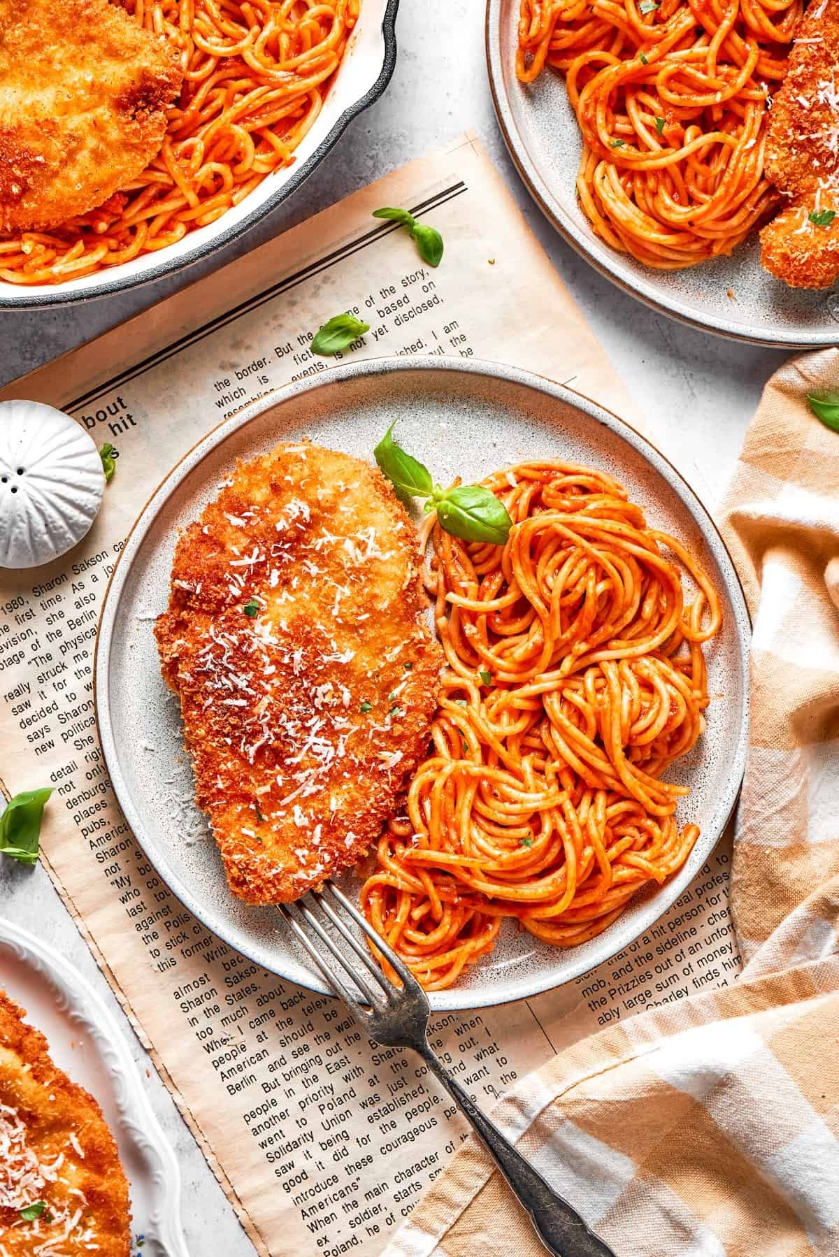 Plates of crusted chicken romano with spaghetti and marinara.