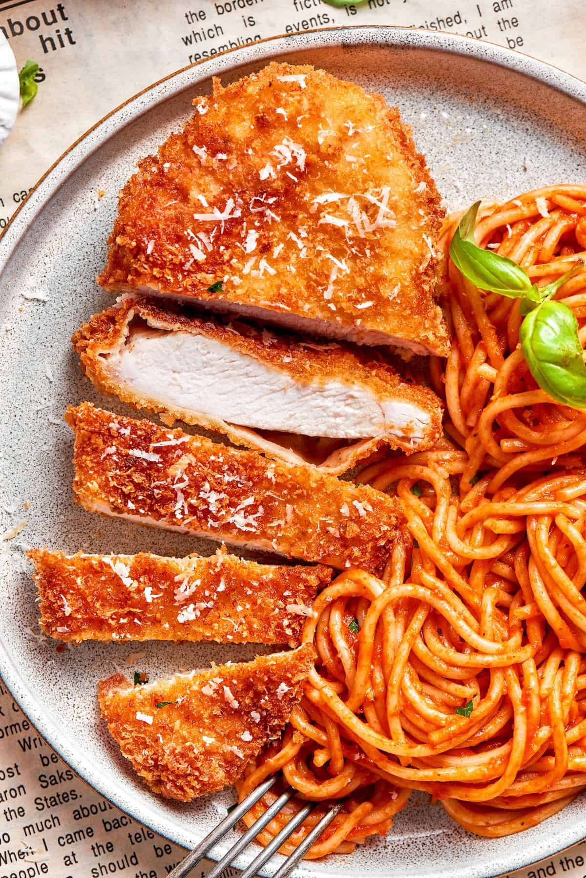 A piece of crusted chicken romano sliced and served with spaghetti.