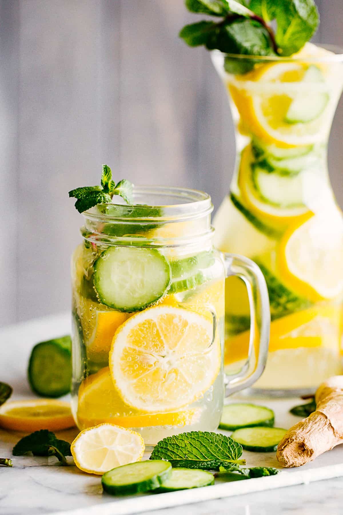lemon cucumber water served in a mason jar with handle, and in a tall carafe