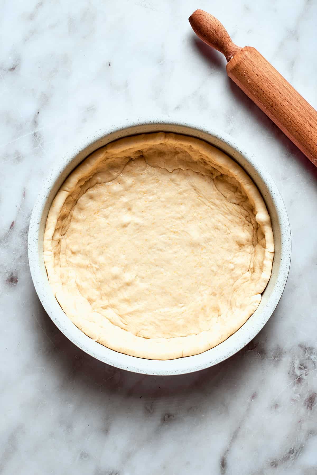 The pizza dough is fitted into a deep sided baking pan.